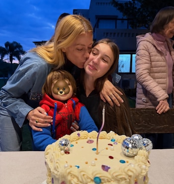 Dos mujeres y un niño con un gráfico sobre el rostro detrás de una torta con una vela y esferas reflectantes sobre la mesa