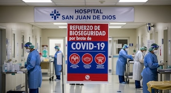 Pasillo de hospital con personal médico usando batas azules, mascarillas y protectores faciales, junto a un cartel rojo sobre bioseguridad y el nombre del hospital.