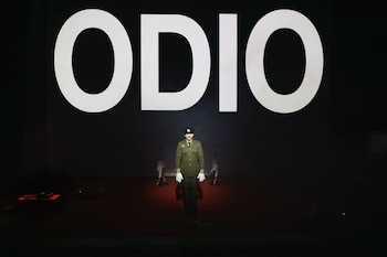 Actor con uniforme militar verde y gorra oscura, con la palabra "ODIO" en letras grandes y blancas al fondo de un escenario