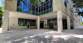 Vista frontal de un edificio moderno con grandes ventanales de vidrio azul y pilares beige, mostrando la entrada a la Oficina del Recaudador de Impuestos
