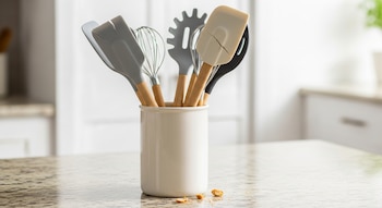 Soporte blanco con utensilios de cocina de silicona y madera; destaca una espátula de goma crema con grietas, sobre encimera de granito en cocina.