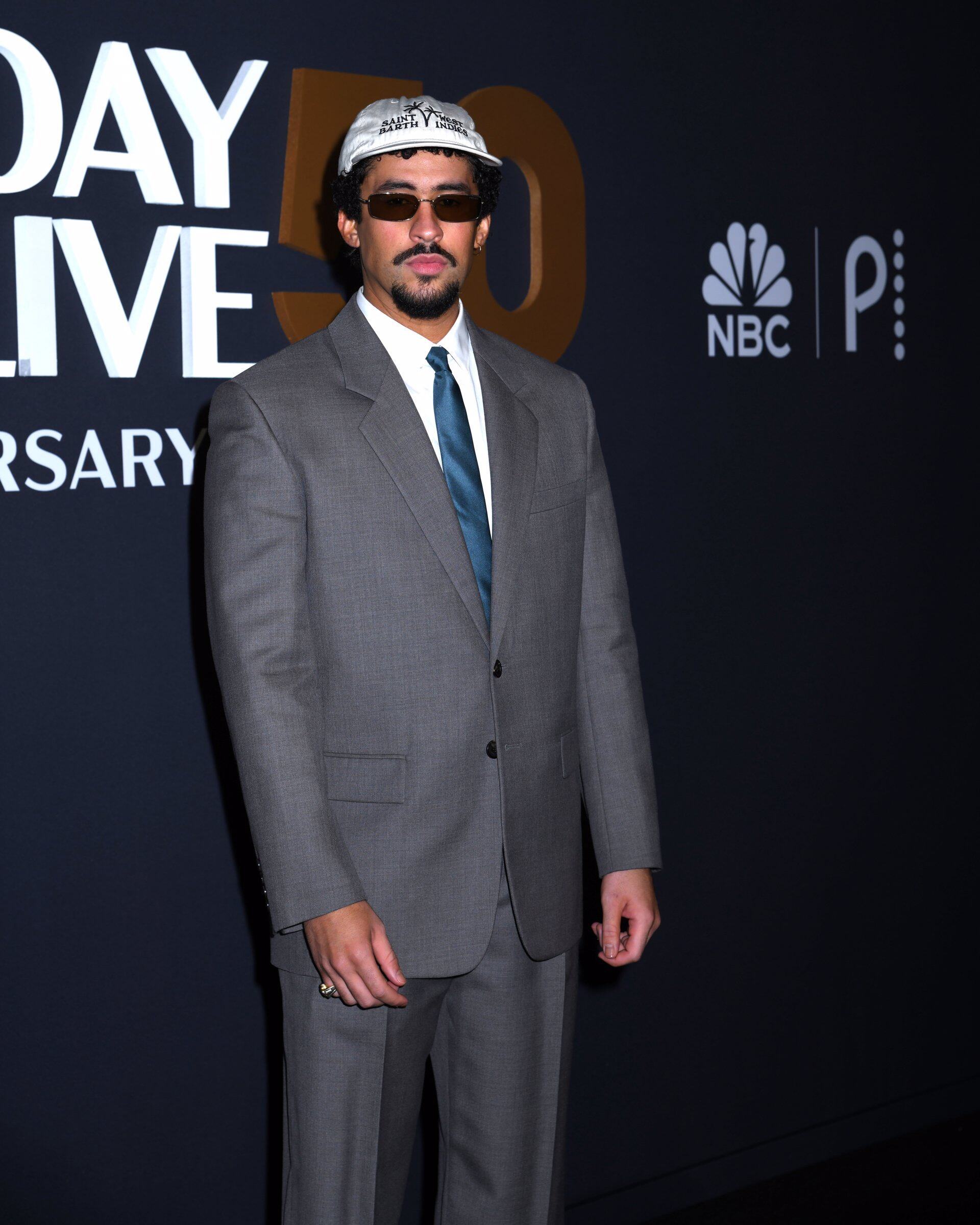 El traje gris clásico combinado con gorra beige y gafas oscuras muestra la versatilidad de Bad Bunny al fusionar sobriedad y actualidad (Image Press)