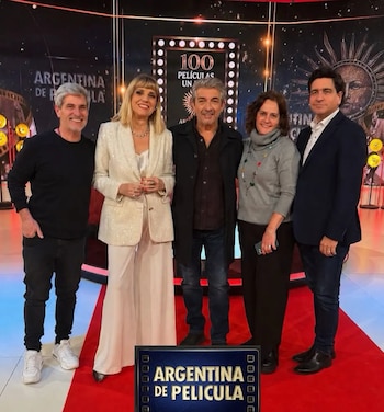 Cinco personas, tres hombres y dos mujeres, posan de pie sobre una alfombra roja en un estudio con el logo de "Argentina de Película"