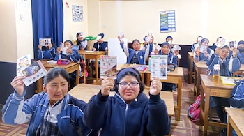 Varias estudiantes dentro de un aula escolar sostienen folletos informativos en sus manos sentadas frente a sus escritorios