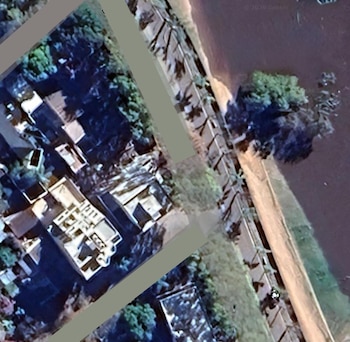 Vista aérea de una zona residencial con casas, árboles y un cuerpo de agua adyacente, con áreas superpuestas en tonos grises