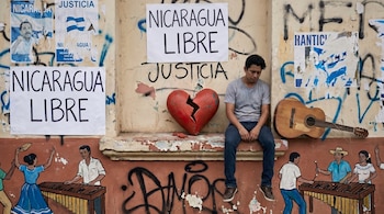 Hombre sentado junto a un corazón roto y una guitarra quebrada, rodeado de paredes con grafitis, carteles de protesta y un mural musical abajo.