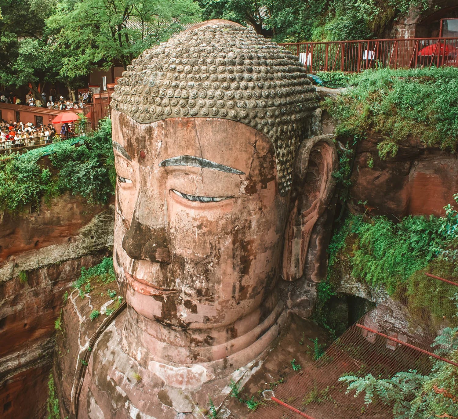 El Gran Buda de Leshan se alza esculpido en un acantilado de piedra en la provincia de Sichuan, donde varios visitantes observan la estructura desde los miradores