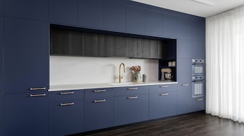 Gabinetes de cocina azul marino, encimera de mármol blanco, fregadero con grifo dorado, gabinetes superiores de roble ennegrecido, horno doble y batidora.
