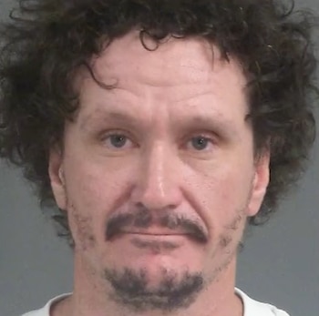 Retrato policial de frente de un hombre con cabello rizado oscuro, bigote y perilla sobre un fondo gris