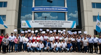 Un grupo grande de hombres y mujeres sonríe y sostiene certificados en alto frente al edificio del Ministerio de Educación de Guatemala con banderas guatemaltecas.
