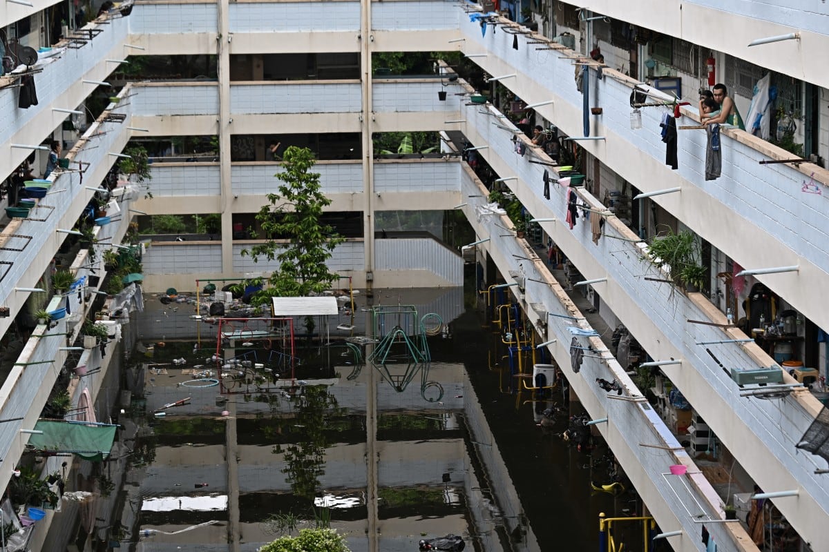 Personas miran el patio inundado de un complejo de viviendas aislado por las aguas en Bang Kapi, Bangkok. Un vecino de 72 años dijo que el agua llegó de noche y sin aviso (Lillian Suwanrumpha/AFP)