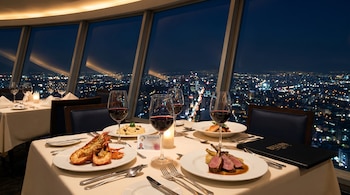 Interior de restaurante de lujo en el WTC de Ciudad de México de noche. Mesa con platos gourmet, copas de vino, credencial INAPAM, y vista nocturna de la ciudad.