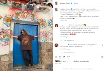 Mujer con camiseta marrón y pantalones oscuros posa frente a una puerta azul. La pared está decorada con murales coloridos. Hay un número 705 sobre la puerta