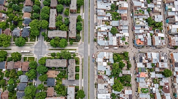 Vista aérea dividida por una vía principal entre una zona residencial arbolada y un sector con viviendas densamente construidas.