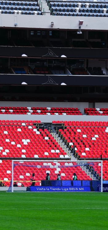 Vista interior de un estadio de fútbol, mostrando el campo de césped verde, una portería y varias secciones de gradas con butacas rojas y blancas