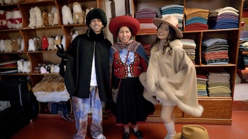 Micro TDH, una mujer con traje tradicional y Wendy Sulca sonríen en una tienda de Cusco. Se ven estantes con textiles y peluches de alpaca