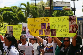 Varias mujeres sostienen pancartas amarillas y blancas con fotos de personas y textos escritos a mano que piden libertad y justicia