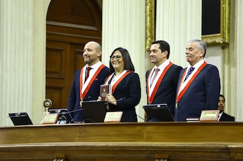 Cuatro personas con traje oscuro y bandas ceremoniales. La mujer central sostiene un libro con "Constitución Política del Perú 1993". Atril de madera al frente