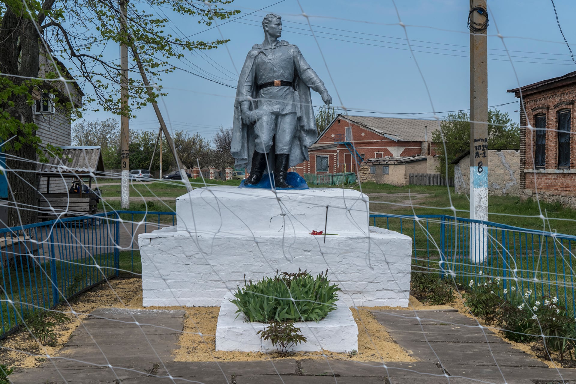 En una aldea ucraniana, se puede ver un monumento a los soldados caídos en la Segunda Guerra Mundial a través de una red antidrones. (Brendan Hoffman/Para The Washington Post)