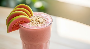 Licuado cremoso y rosado de guayaba y avena en vaso alto, decorado con rodajas de guayaba y avena espolvoreada, con un fondo luminoso y natural.