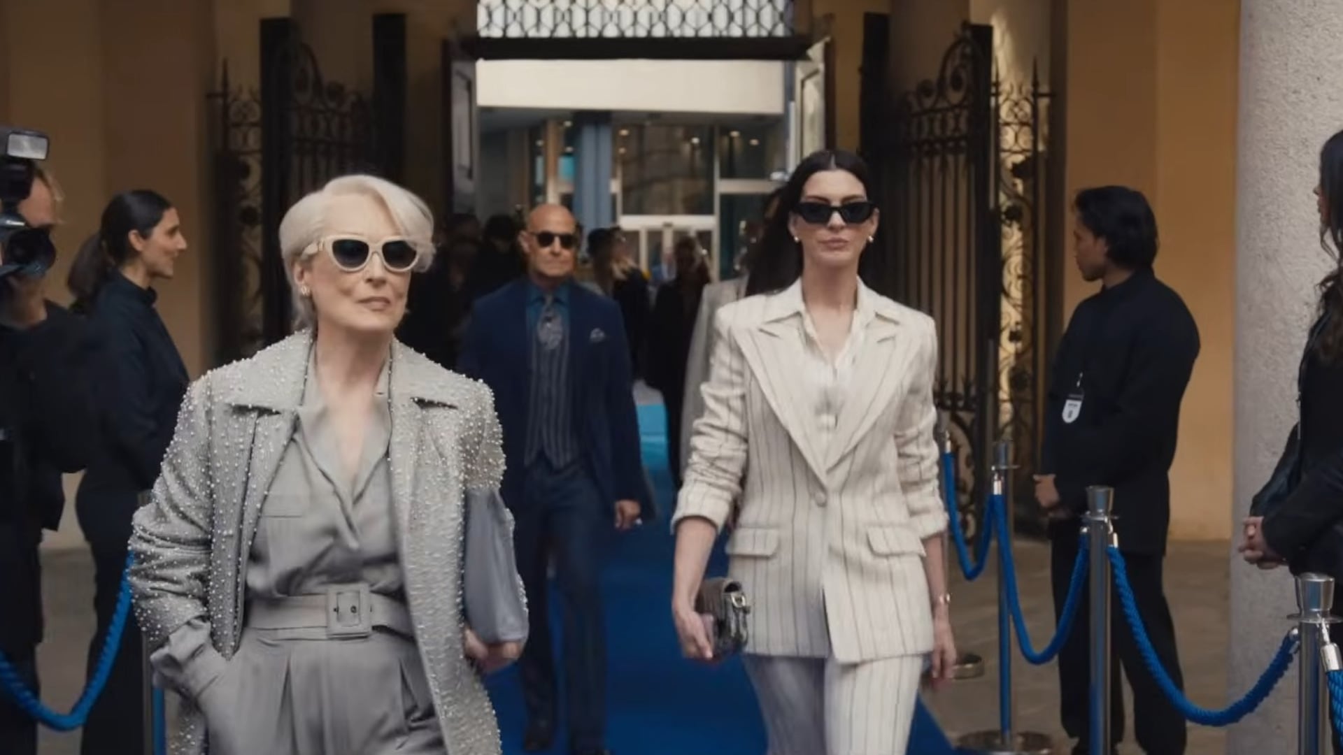 El traje de lino claro con rayas verticales proyecta poder ejecutivo y brillo sofisticado en la alfombra azul (Captura de tráiler oficial)