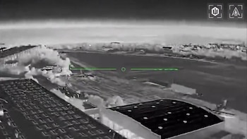 Vista aérea termográfica de una explosión con denso humo en una pista de aterrizaje o instalación industrial. Se aprecian edificios en primer plano