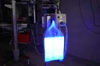 Dispositivo de fototerapia médica BiliSoft 2.0 encendido con luz azul, conectado a equipo hospitalario en una habitación de hospital