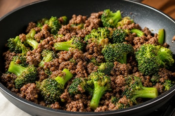 Carne picada cocida y ramilletes de brócoli verde mezclados dentro de una sartén negra.