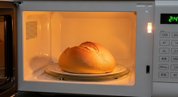 Un pan redondo de color dorado sobre un plato blanco dentro de un microondas encendido, con la luz interior brillante y la pantalla mostrando '2:4'.