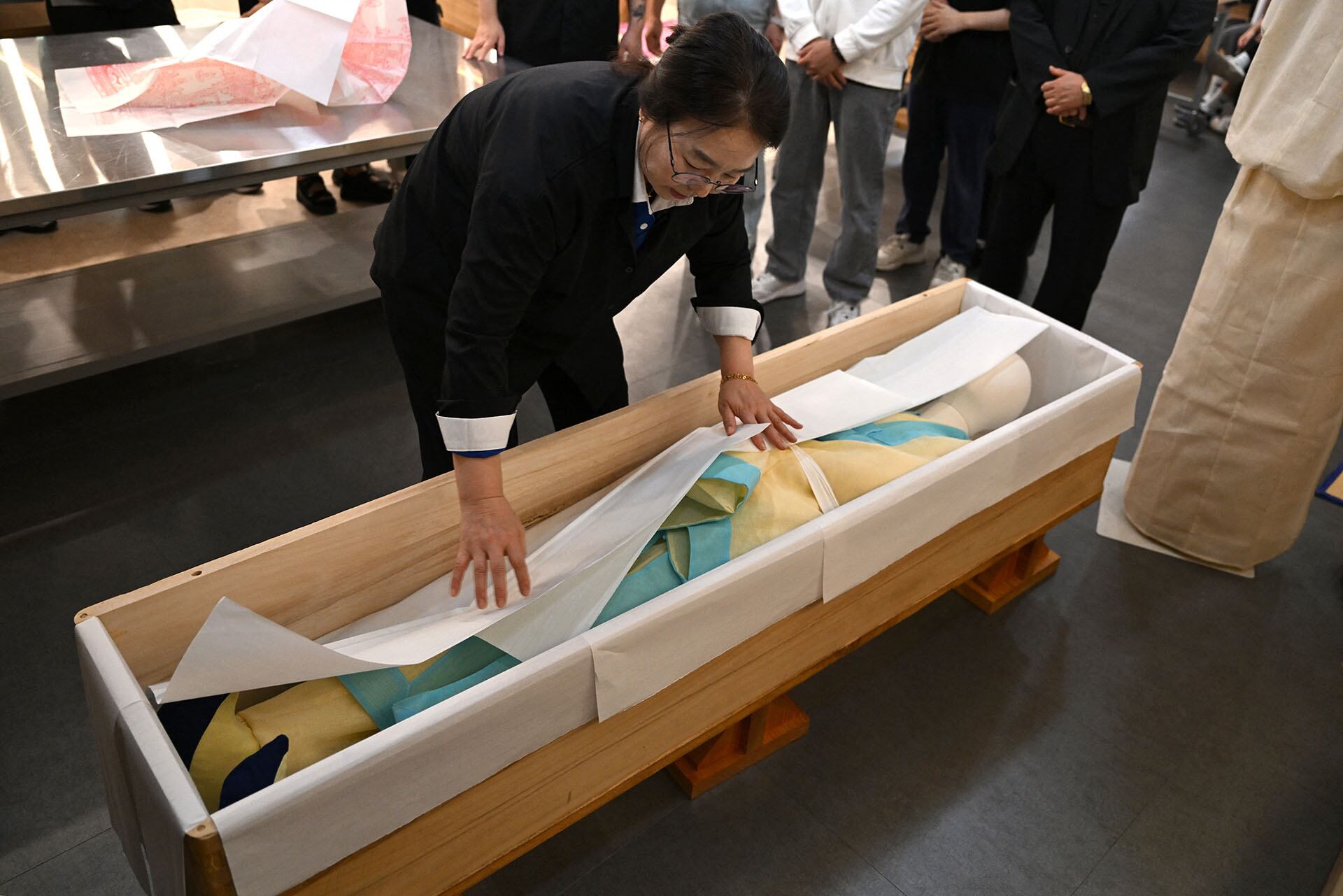Un instructor da los últimos retoques a un maniquí vestido con una tela funeraria tradicional coreana para convertirlo en un ataúd durante una clase de administración funeraria en el Instituto de Ciencia y Tecnología de Busan. (Foto de Jung Yeon-je / AFP)