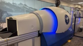 Un escáner de equipaje de la TSA blanco y azul con iluminación LED sobre una cinta transportadora en una sala aeroportuaria