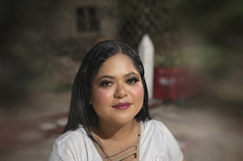 Mujer con cabello largo oscuro, maquillaje de ojos, pestañas postizas, rubor y labios oscuros. Fondo desenfocado.
