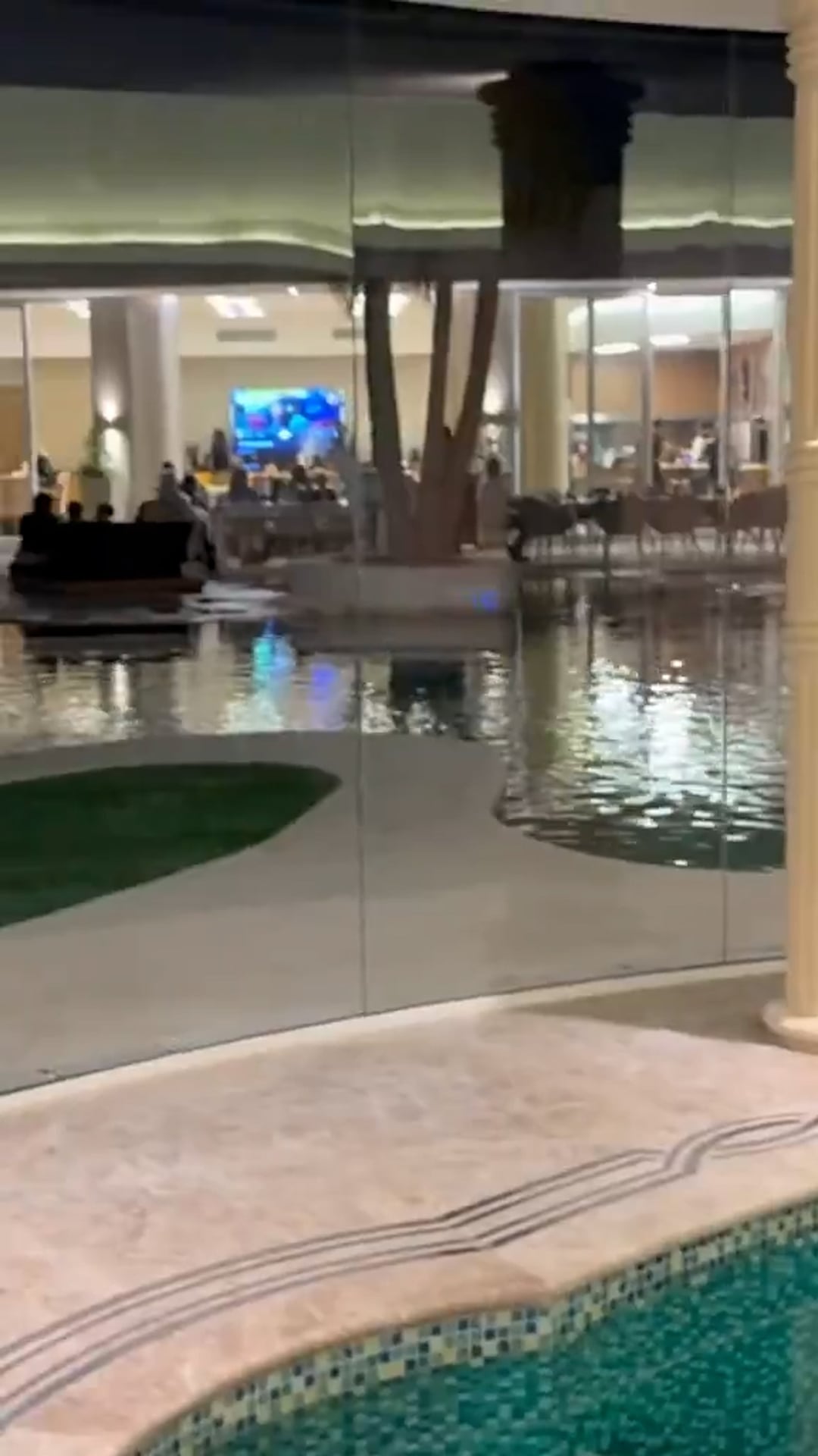 Una vista nocturna revela el sofisticado diseño interior y exterior de la mansión de Carlos Tevez, con un estanque reflectante y un espacio social elegante.