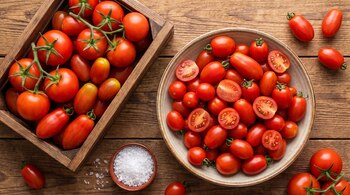 Caja de madera con tomates, cuenco de cerámica con tomates enteros y partidos, pequeño recipiente con sal marina sobre mesa de madera.