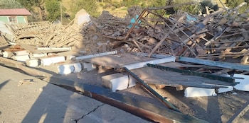 Pila de escombros de una estructura colapsada, incluyendo madera, ladrillos, cemento y metal, bajo un cielo claro con árboles al fondo