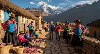 Grupo de personas con vestimenta tradicional y visitantes en un camino de piedra entre casas de paja, con montañas nevadas al fondo y objetos artesanales.