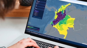 Una persona usa un computador portátil que muestra un mapa interactivo de Colombia con divisiones de colores y opciones de filtro.
