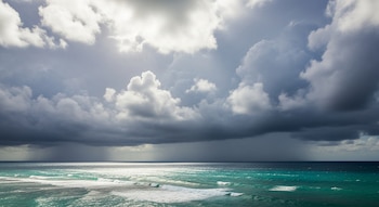 Cielo cubierto de nubes grises y blancas sobre el mar Caribe colombiano. Se observa una cortina de lluvia a lo lejos, sobre aguas turquesas con olas espumosas.