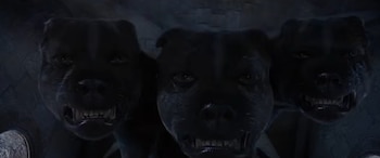 Tres cabezas de un perro negro de gran tamaño muestran sus dientes en un espacio de piedra en penumbra