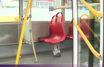Interior de un bus del Metropolitano con un asiento rojo de plástico desprendido y barandas amarillas, mostrando daños materiales visibles
