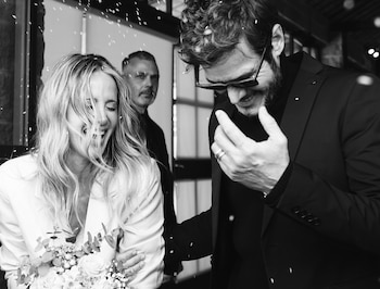 Fotografía en blanco y negro de una mujer con ramo de flores y un hombre con traje que sonríen mientras les cae confeti