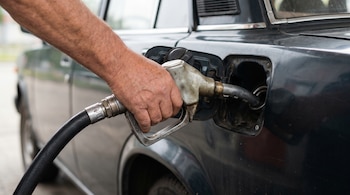 Primer plano de una mano sosteniendo una boquilla de combustible insertada en el tanque de gasolina abierto de un coche oscuro.