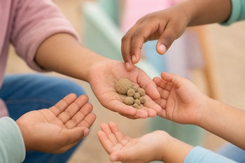 Varias manos infantiles abiertas sostienen y rodean pequeñas bolitas hechas de arena.