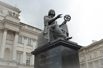 La estatua se sitúa en un pedestal, mostrando al científico sentado con orbe que describe las órbitas de los planetas en una mano y la otra la tiene extendida enfrente de él