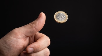 Una mano lanza una moneda de un euro al aire para decidir un cara o cruz.