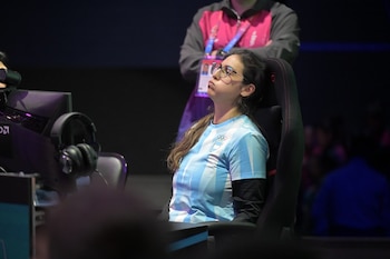 Una mujer con gafas y camiseta de la delegación argentina mira hacia arriba sentada en una silla de escritorio frente a un monitor