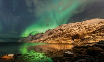 Aurora boreal iluminando el cielo de Tromsø con paisaje nevado