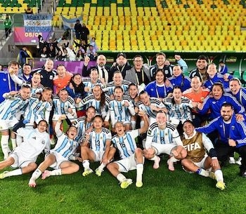 Jugadoras y cuerpo técnico del equipo femenino de fútbol de Argentina posan juntos y sonrientes sobre el césped de un estadio