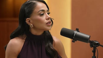 Onelia Molina, una mujer con cabello oscuro y un top morado, habla frente a un micrófono negro en un estudio con paredes marrones