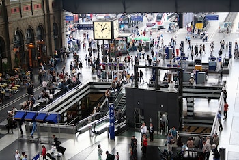 Vista aérea de la concurrida Zürich Hauptbahnhof con múltiples niveles, gente caminando, escaleras mecánicas, un gran reloj y trenes en las vías superiores